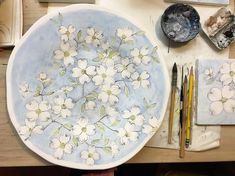 a plate with flowers painted on it next to paintbrushes and other art supplies