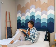 a woman sitting on top of a bed reading a book in front of a colorful wall