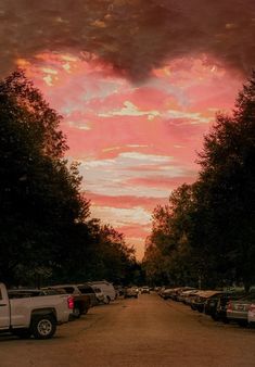 the sky is pink and orange as cars are parked on the side of the road