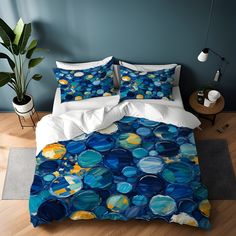 a bed with blue, yellow and white circles on the comforter is next to a potted plant