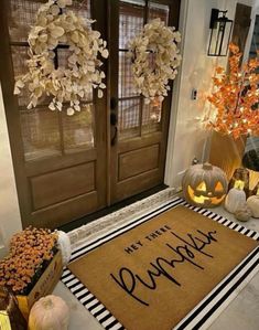 a welcome mat on the front porch with pumpkins and other decorations in front of it