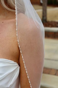 the back of a bride's wedding dress with pearls on her shoulder and veil