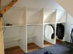 an attic bedroom with white shelving and clothes on hangers in front of the closet