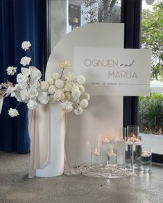 white flowers and candles are in vases next to a sign