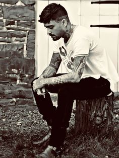 a man with tattoos sitting on top of a tree stump in front of a building