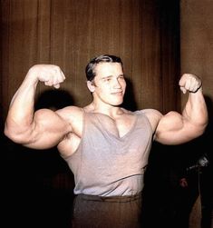 a man flexing his muscles while standing in front of a wooden paneled wall