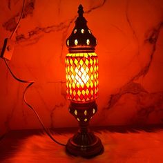 a red and yellow lit lamp on a table next to a marble wall behind it