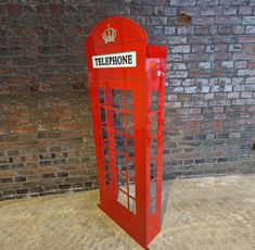 a red phone booth sitting in front of a brick wall