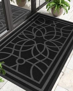 a black door mat on the outside of a house with potted plants next to it