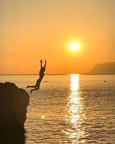 a person jumping into the water from a cliff in front of an orange and yellow sky