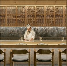 a man sitting at a long table in front of a wall with carved screens on it