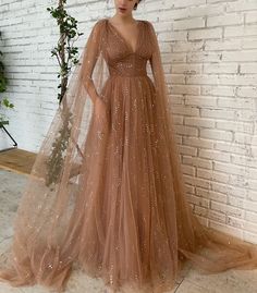 Details:- Tulle fabric with glittering flowers- Desert-sands hue- Draped bodice- Elegant narrow V-shaped neckline- Cinched waist with boning- A-line silhouette- Inseam pockets- Floor-length- Wide gathered skirt with a court train- Long c... Prom Dress With Pockets, Teuta Matoshi, Detachable Cape, Sweep Train Prom Dress, Sparkly Prom Dress, Prom Dresses With Pockets, Tulle Sleeves, Beautiful Prom Dresses, فستان سهرة