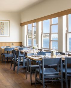 an empty restaurant with blue chairs and wooden tables overlooking the ocean in front of large windows