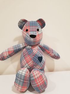 a plaid teddy bear sitting up against a white wall with a heart on it's chest