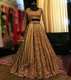 a gold gown on display in front of a black chair and window with curtains behind it