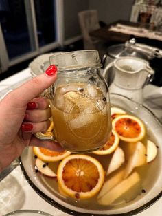 a person holding a mason jar filled with liquid and sliced oranges on a plate