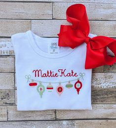 This adorable girl's shirt is perfect for Christmas and would be a super cute outfit for a Christmas card! The detailed design of the Christmas Ornaments, as well as your chosen name, is created by machine embroidery and uses high quality thread.  The white shirt is true to size and is made out of 100% combined cotton interlock fabric to keep your child completely comfortable. The shirt has naturally tapered shoulders and includes a ruffled hemline. The short sleeve shirts have puff sleeves.  Pl White Tops With Custom Embroidery For Christmas, Holiday Cotton Top With Embroidery, Holiday Cotton Embroidered Tops, Christmas White Embroidered Tops, Embroidered Christmas Holiday Tops, White Christmas Tops With Embroidered Graphics, Christmas Cotton Top With Embroidered Text, Holiday Embroidered Tops As Gift, Holiday Embroidered Cotton Top