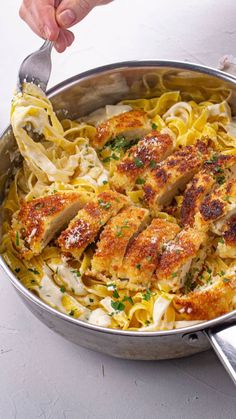 someone is holding a fork over some pasta in a pan with chicken and parmesan cheese