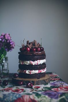 a chocolate cake with cherries and whipped cream on top sitting on a table next to flowers