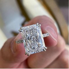 a person holding an engagement ring with a large cushion cut diamond in it's center