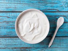 a bowl of yogurt and two spoons on a blue wooden table top