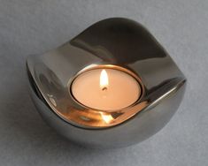 a lit candle in a metal bowl on a gray surface with the light shining through it