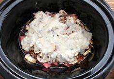 a slow cooker filled with meat and gravy on top of wooden table