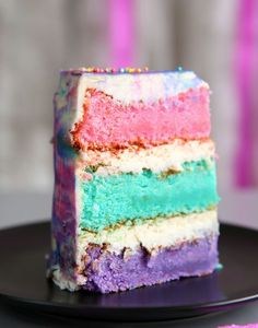 a slice of rainbow cake sitting on top of a black plate with pink and blue frosting