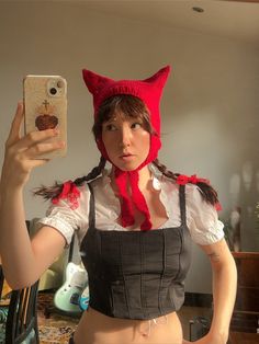 a woman taking a selfie in front of a mirror wearing a red cat hat