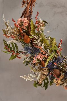 an arrangement of flowers and plants hanging from a ceiling fixture in front of a wall