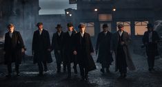 men in trench coats and hats walking through an old town at night with lights on