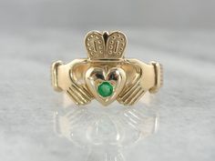 A pretty, shining emerald has been set perfectly just in the center of this vintage ring. The color of the gold, rich and warm, is a perfect counterpoint to this lovely stone.Betrothal rings depicting two clasped hands date back many centuries in European history. The Irish version, the Claddagh ring, came about in the 1600's and has been produced continually since that time. Metal: 14 Karat Yellow GoldCrown To Heart Width: 14.5 mmGem: EmeraldGem Measurement: 2.88 mm, roundMarks: Although not st Clasped Hands, Claddagh Ring, Emerald Gem, Claddagh Rings, European History, Gold Crown, Vintage Ring, Hand Engraving, New Hampshire