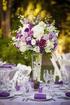 a vase filled with purple and white flowers sitting on top of a table covered in glasses