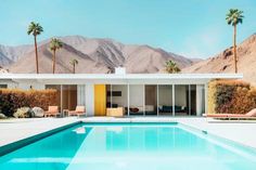 a swimming pool surrounded by palm trees in front of a house with mountains in the background