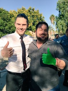 two men standing next to each other giving the thumbs up sign with green gloves on