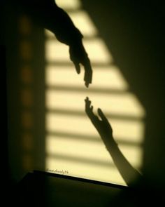 two hands reaching towards each other in front of a window with the light coming through