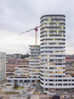 a tall white building with lots of windows and lights on it's sides in front of a cityscape