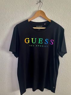 a black t - shirt with the word guess printed on it hanging from a hanger