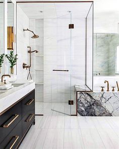 a white bathroom with marble counter tops and gold accents on the shower door, sink, and bathtub