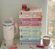 a stack of books sitting on top of a table next to a cup