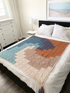 a bed with a crocheted blanket on top of it next to a dresser