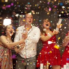 three people standing in front of confetti while one person holds up a cell phone