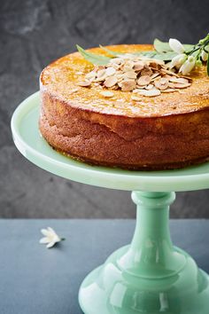 a cake sitting on top of a green plate with almonds and leaves around it