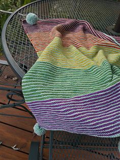 a multicolored knitted blanket sitting on top of a metal table next to a chair