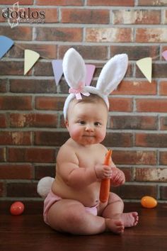 a baby sitting on the floor with a carrot in her hand and bunting ears