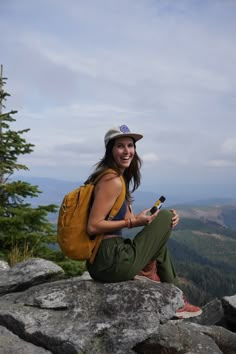 a woman sitting on top of a large rock with a cell phone in her hand