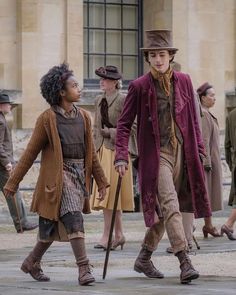 two children dressed in period clothing walking down the street with an older man and woman