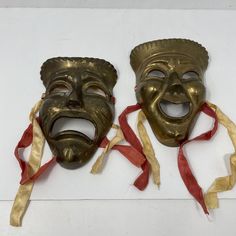 two masks with ribbons tied around them on a white surface, one is gold and the other is red