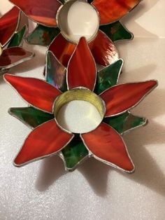 two red and green stained glass ornaments on a white table top, one with a candle holder in the shape of a poinsettie