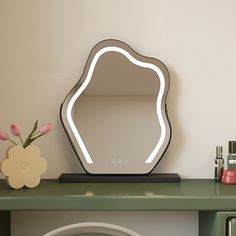 a mirror sitting on top of a green desk next to a vase with pink flowers